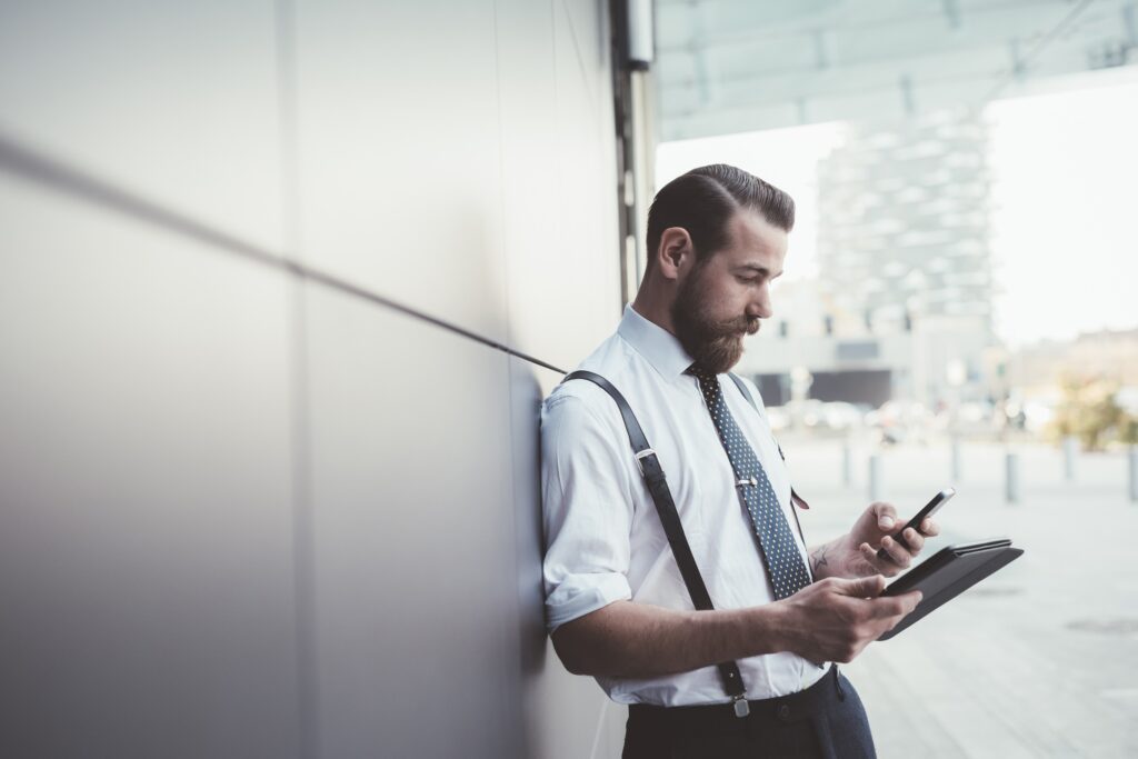 Stylish businessman using smartphone and digital tablet outside office